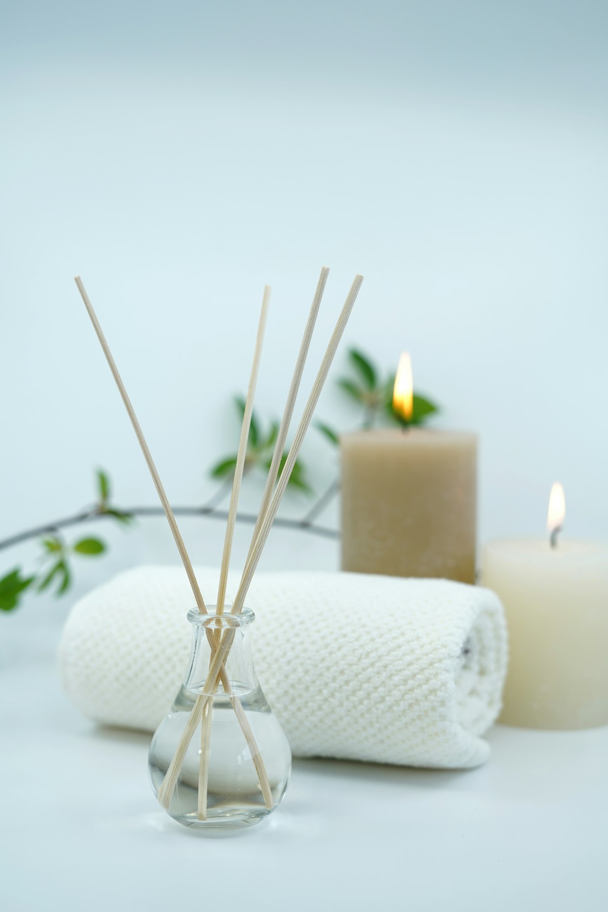 Soft rolled towels, a reed diffuser and a candle in a peaceful spa setting